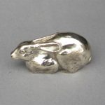 A silver sculpture of a small crouching hare