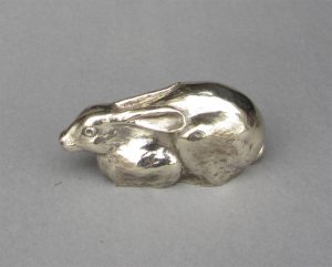 A silver sculpture of a small crouching hare